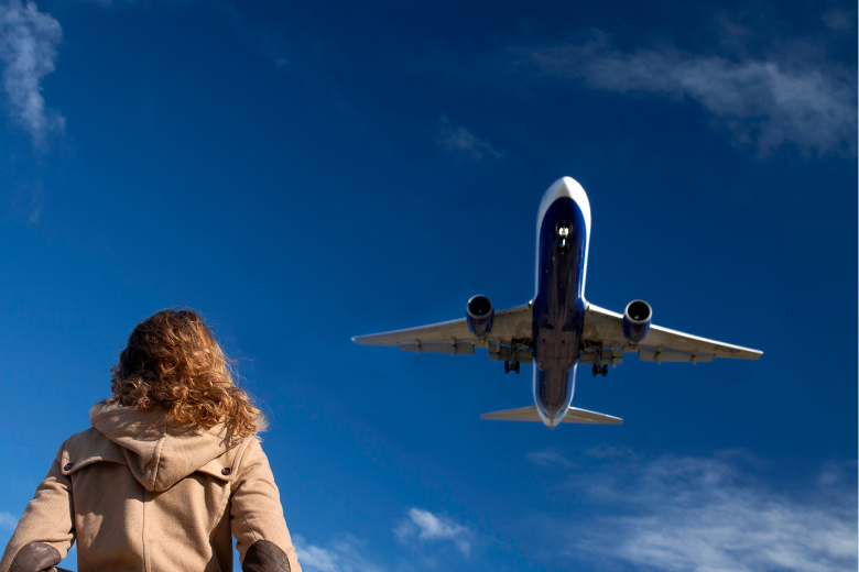 Kvinna kollar upp mot ett flygplan i himmeln 