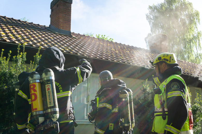 Tre brandmän med utrustning står utanför ett hus och pratar