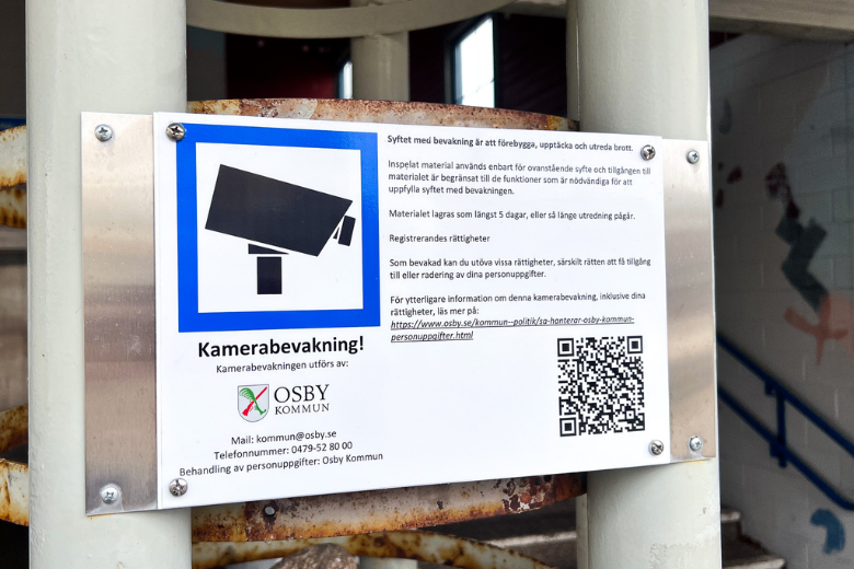 Skylt på en stolpe utomhus med information om kamerabevakning