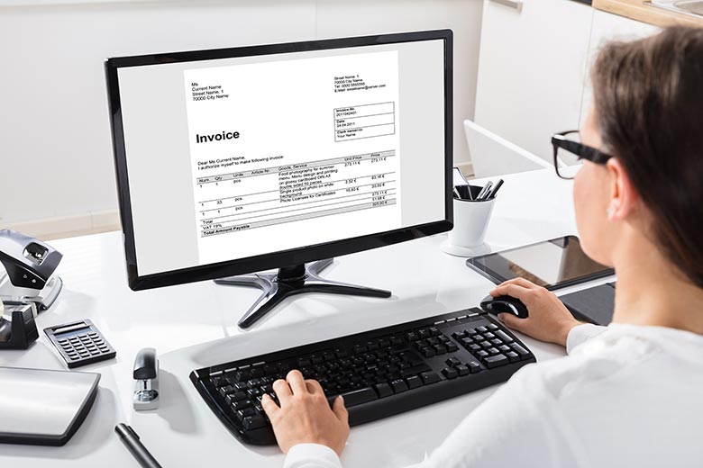 Kvinna sitter vid dator och läser ett dokument som syns på skärmen, det är en räkning.
