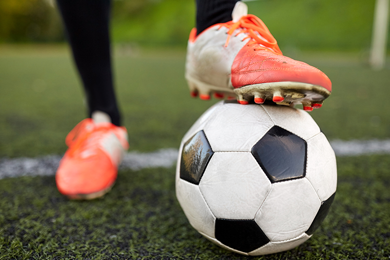 En fotboll som står på en fotbollsplan. På bollen vilar en orange sko